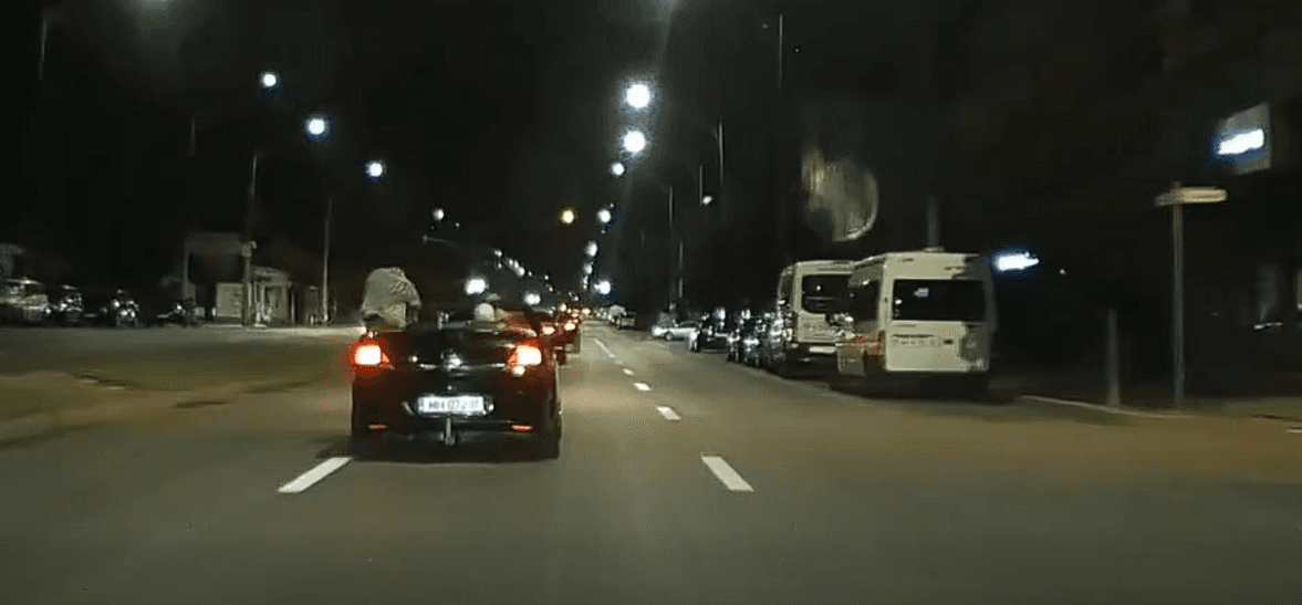 Maşină decapotabilă, aparent lăsată să ruleze din inerţie, pe un buleverd din Drobeta Turnu Severin. Persoana aflată pe locul şoferului lasă volanul şi se ridică în picioare